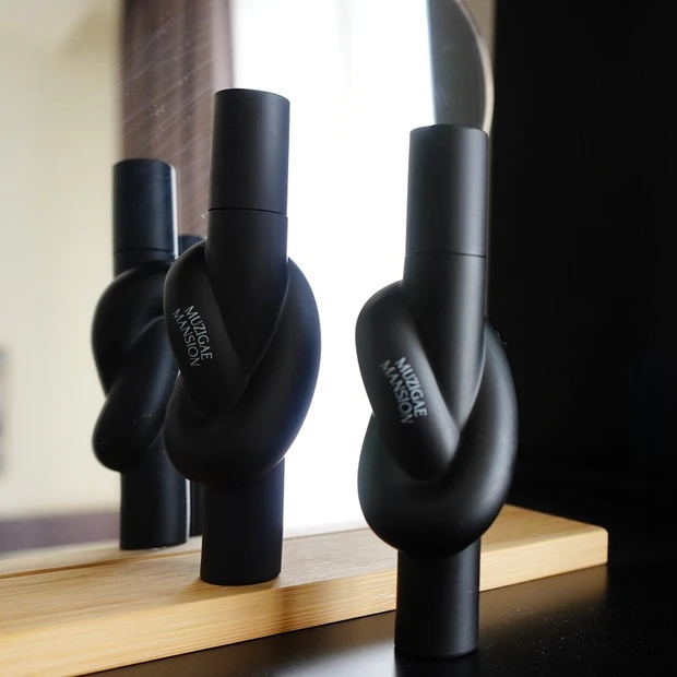 MUZIGAE MANSION（ムジゲマンション）のタイアップカバーティント2本が鏡の前に立てかけられた写真。特徴的なノットデザインが美しく映える構図。