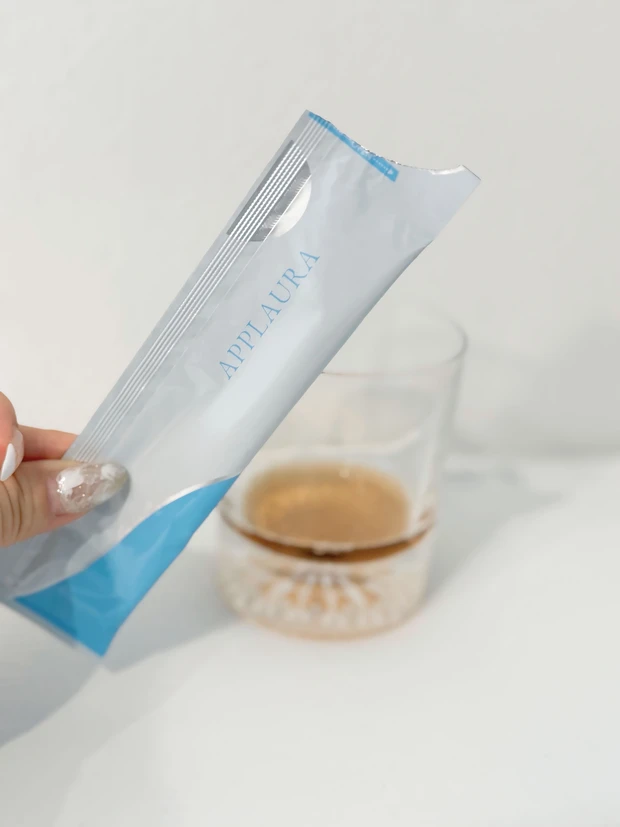 APPLAURA(アプローラ)のLACTULOSE SENSOR®の個包装スティックから、グラスに中身を注いでいる様子。透明なグラスに淡いブラウン色の液体が入っている。